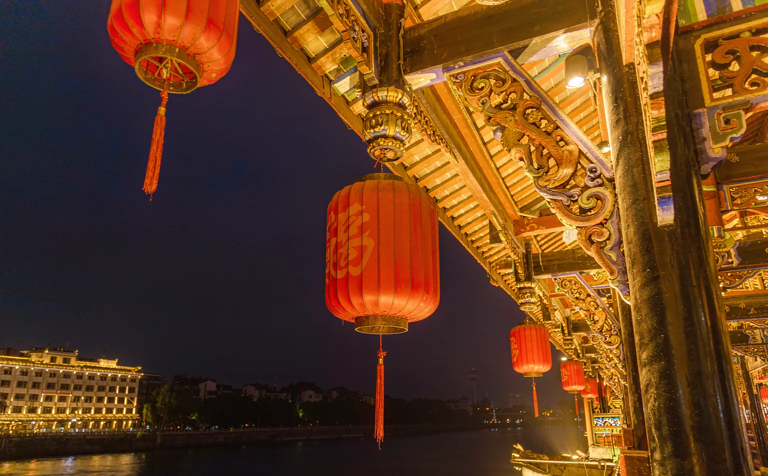 Traditional lanterns and wooden carvings under the pavilion roof of Anshun Bridge at night