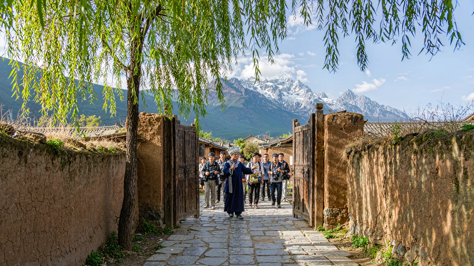 Tour group entering Baisha Ancient Town with mountain backdrop