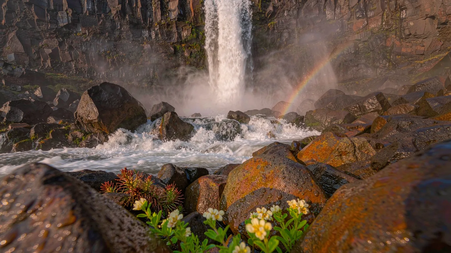 Close-up of mist and rainbow at base of Changbai Waterfall with mossy rocks