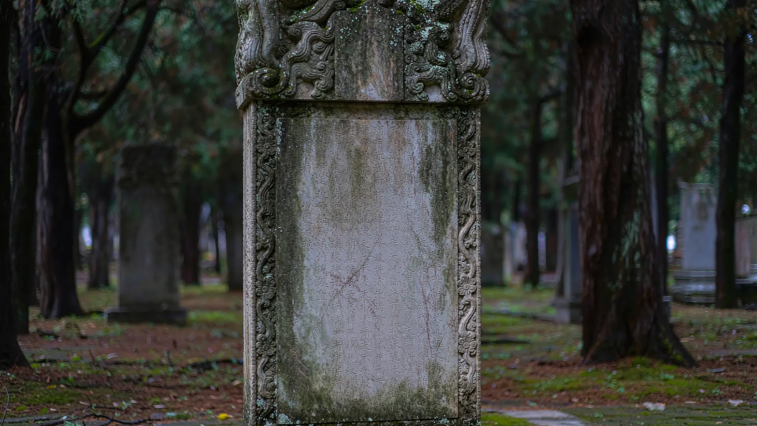 Weathered stone tombstone with ancient Chinese inscriptions in cemetery