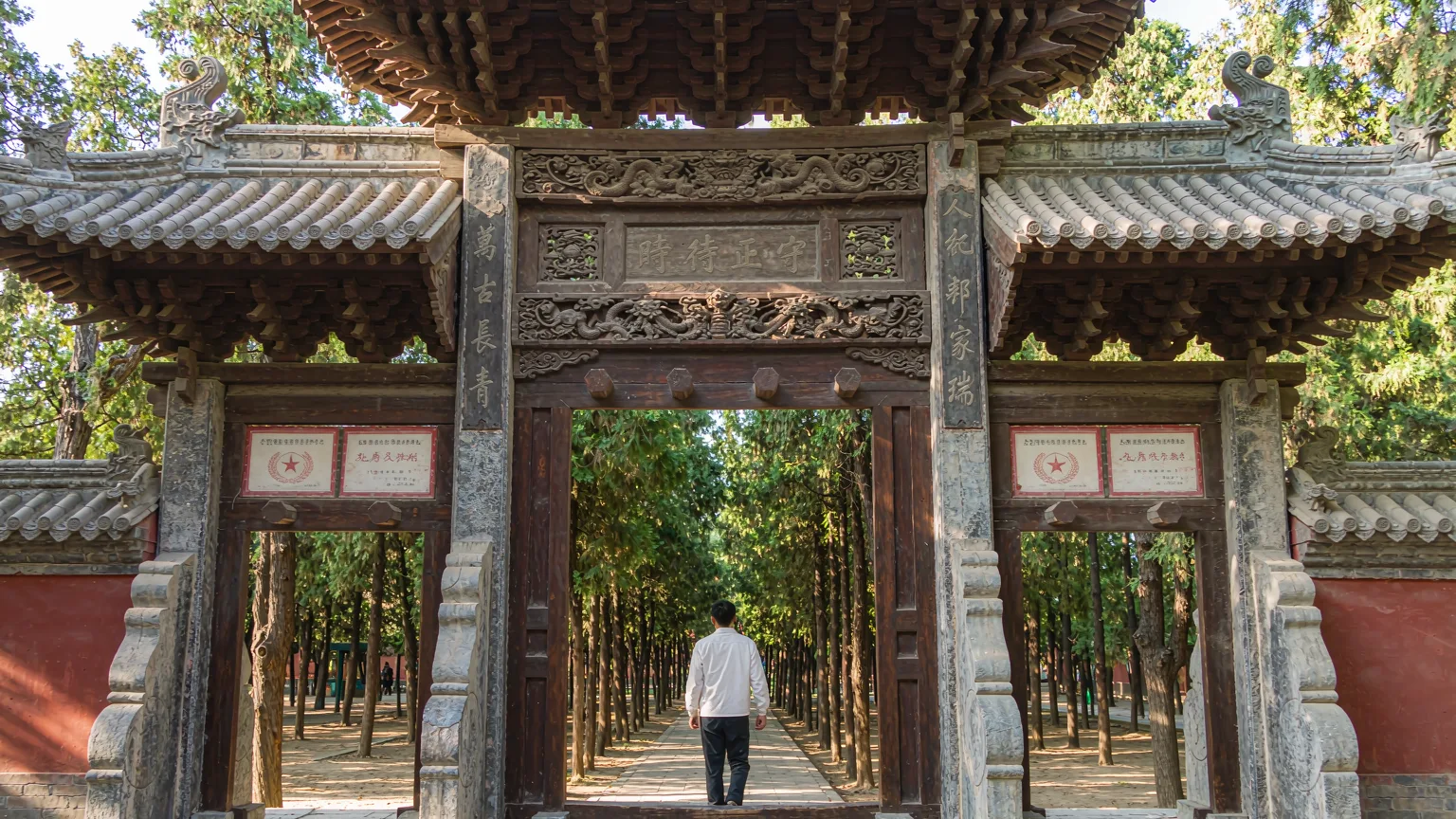 Visitor entering cemetery through ornate traditional stone gateway
