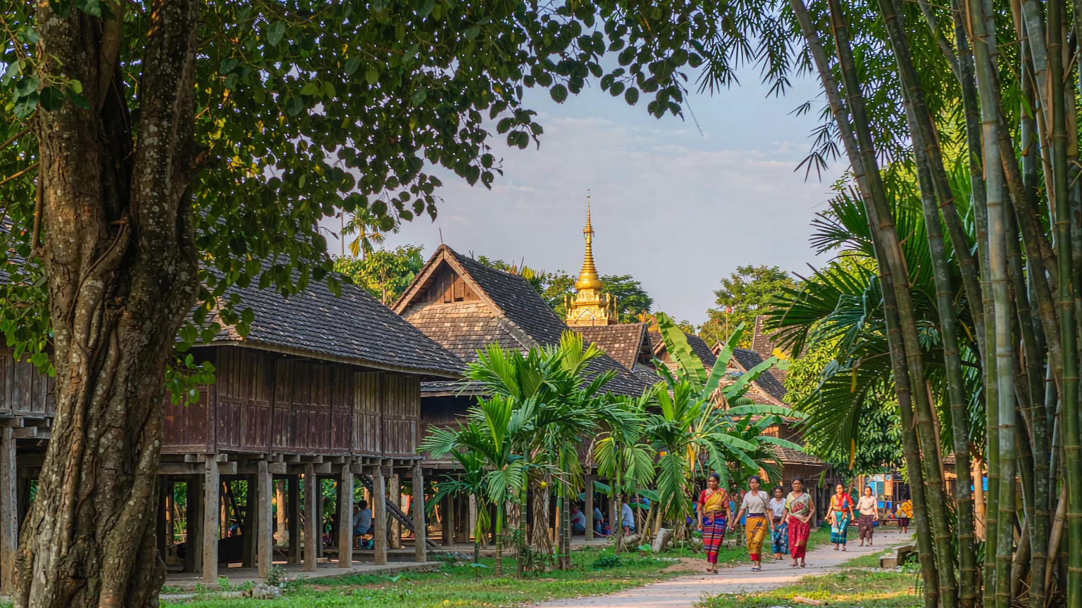 Dai women in sarongs walking among stilted houses in Dai Park
