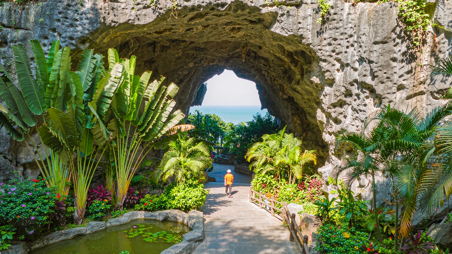 Tourist walking stone path under Small Grotto Heaven arch, ocean ahead