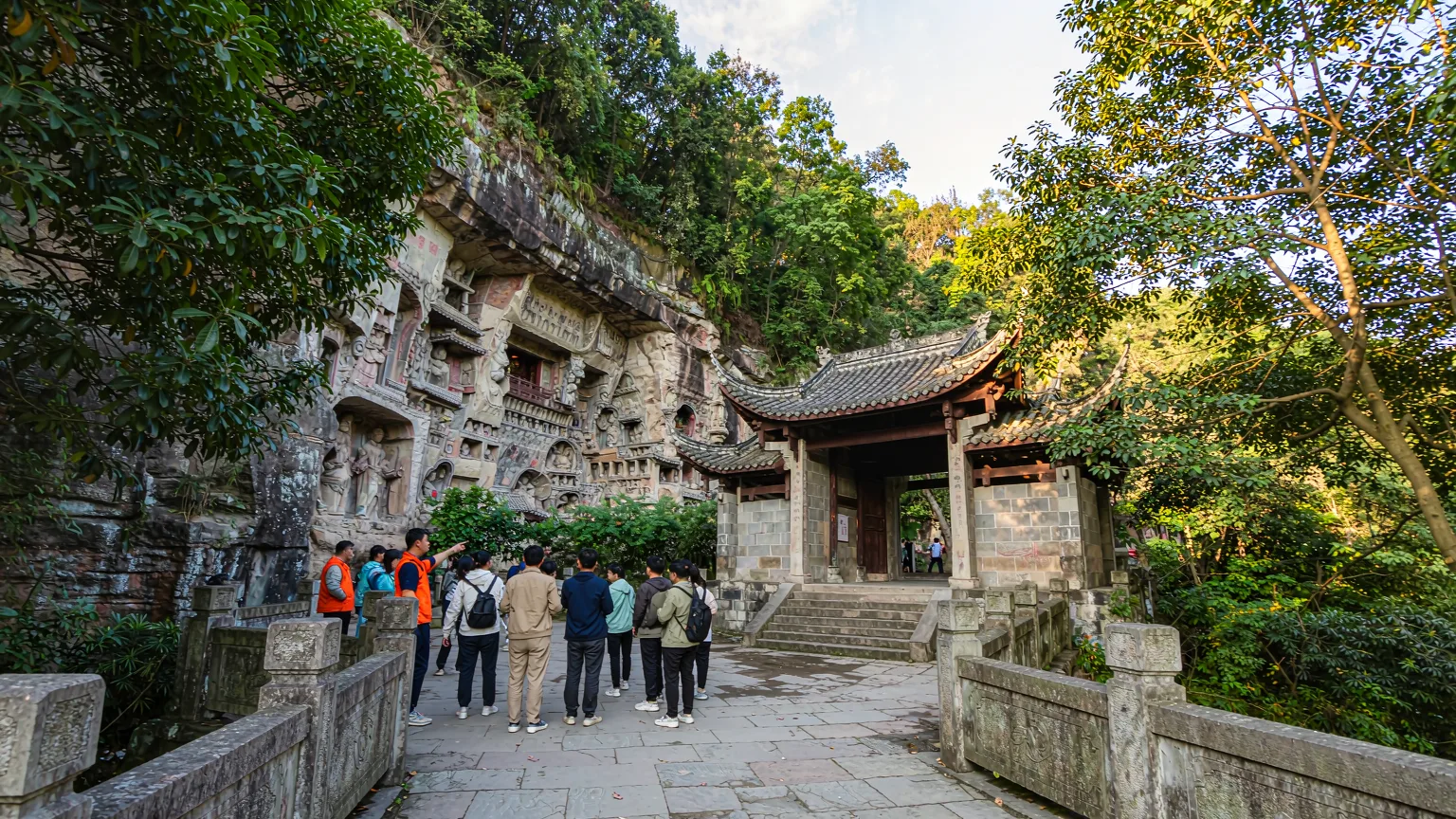 Tourists on a stone path approaching Baodingshan carvings entrance.