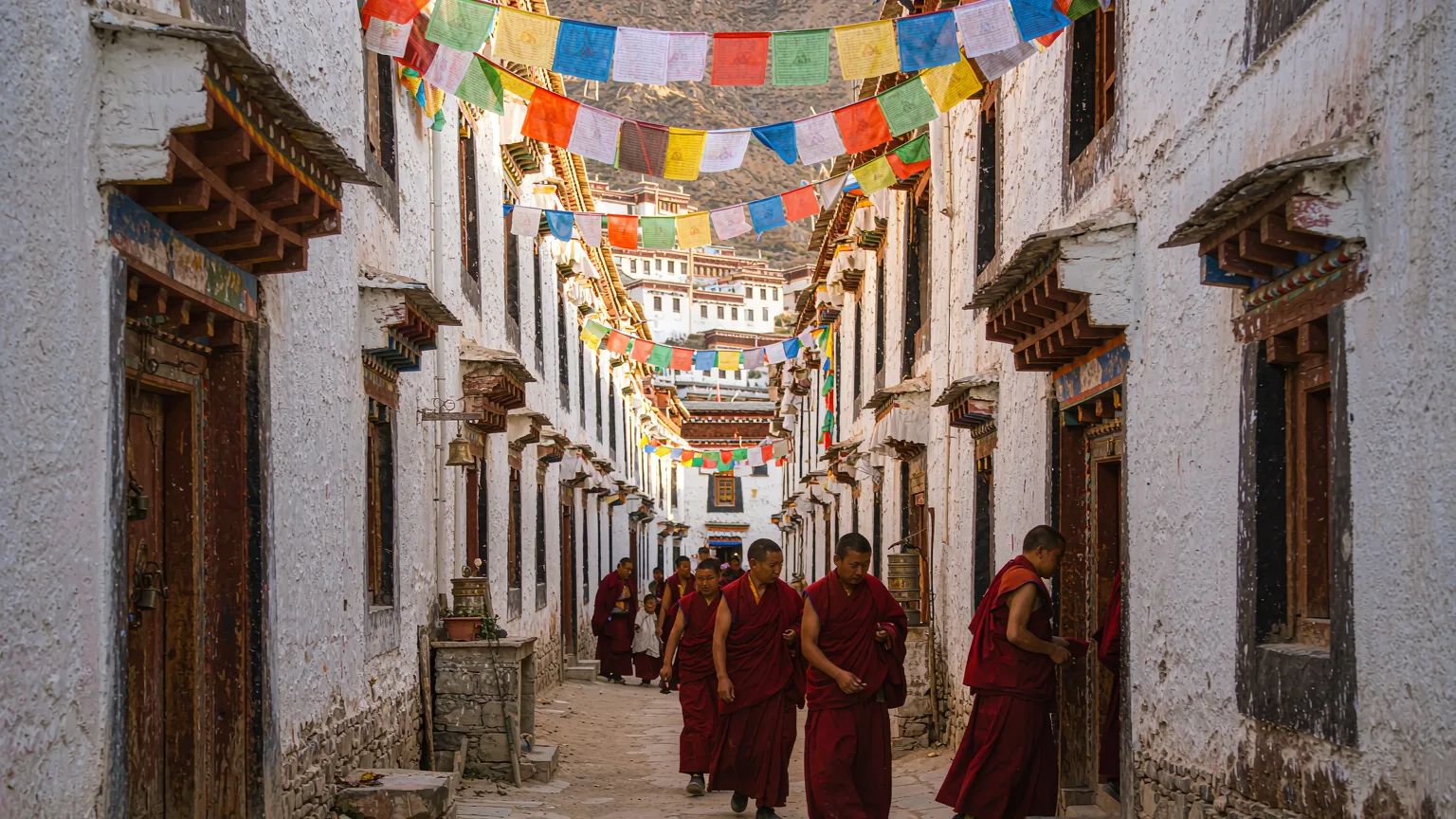 Monks in crimson robes walking through a whitewashed alley at Drepung Monastery