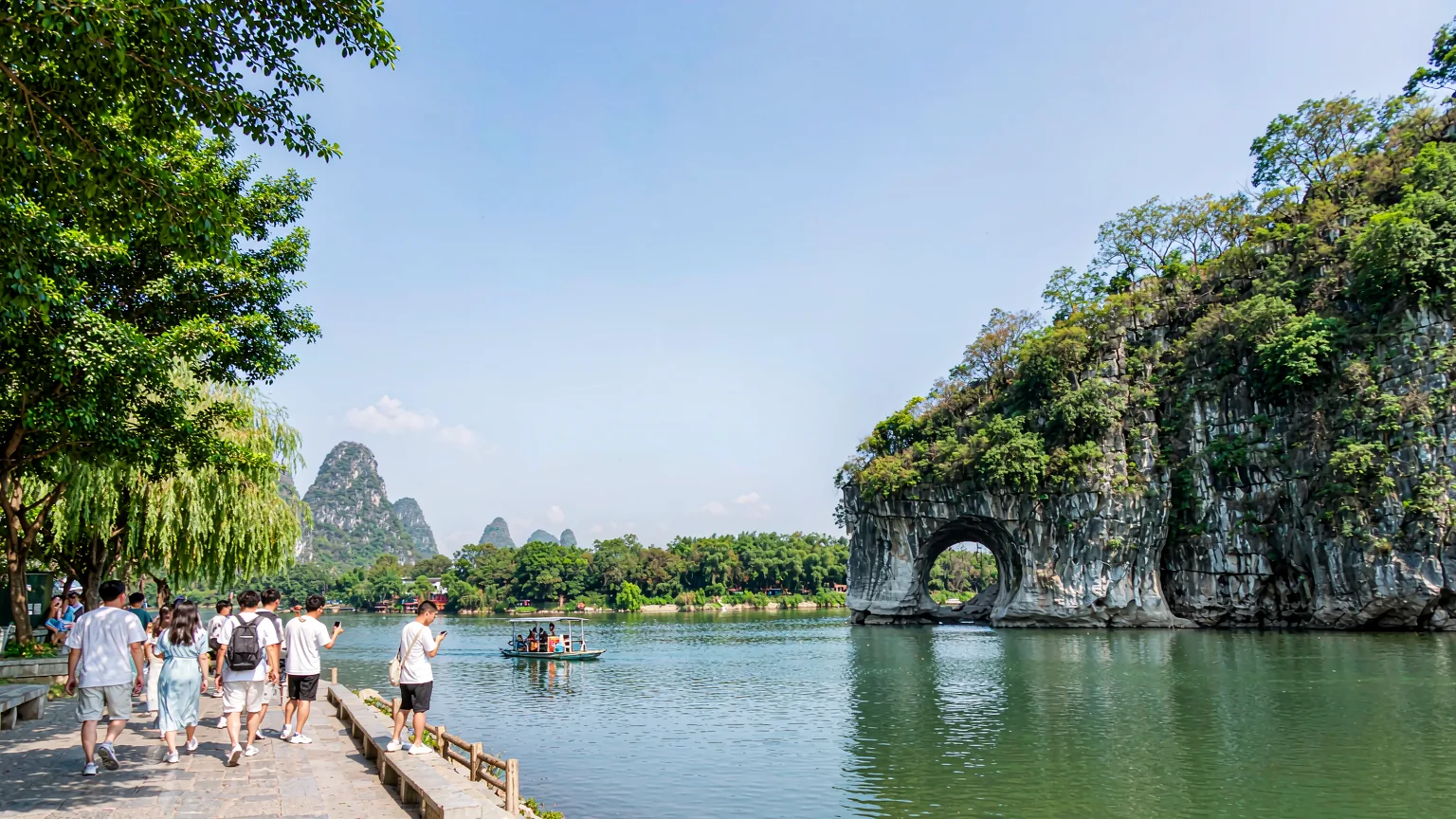 Tourists on riverside path with boat and Elephant Trunk Hill in background