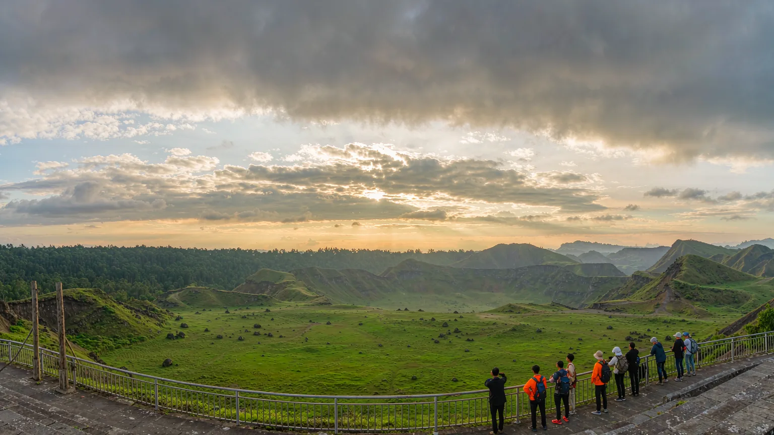 Visitors on crater rim overlook green caldera and volcanic cones panorama