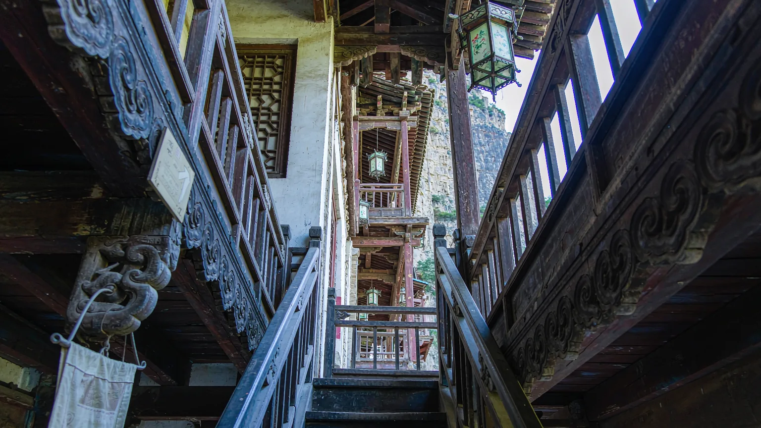 Visitors climbing narrow wooden staircase inside Hanging Temple with cliff views
