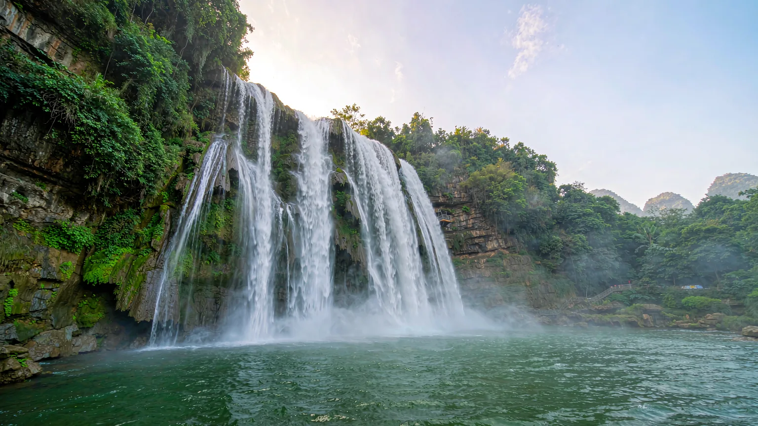 Panoramic view of Huangguoshu Waterfall cascading into turquoise pool amid karst landscape