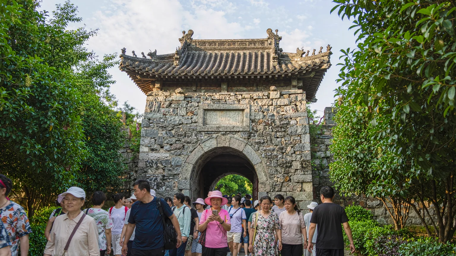 Tourists entering Hulishan Fortress through historic stone gatehouse with guide