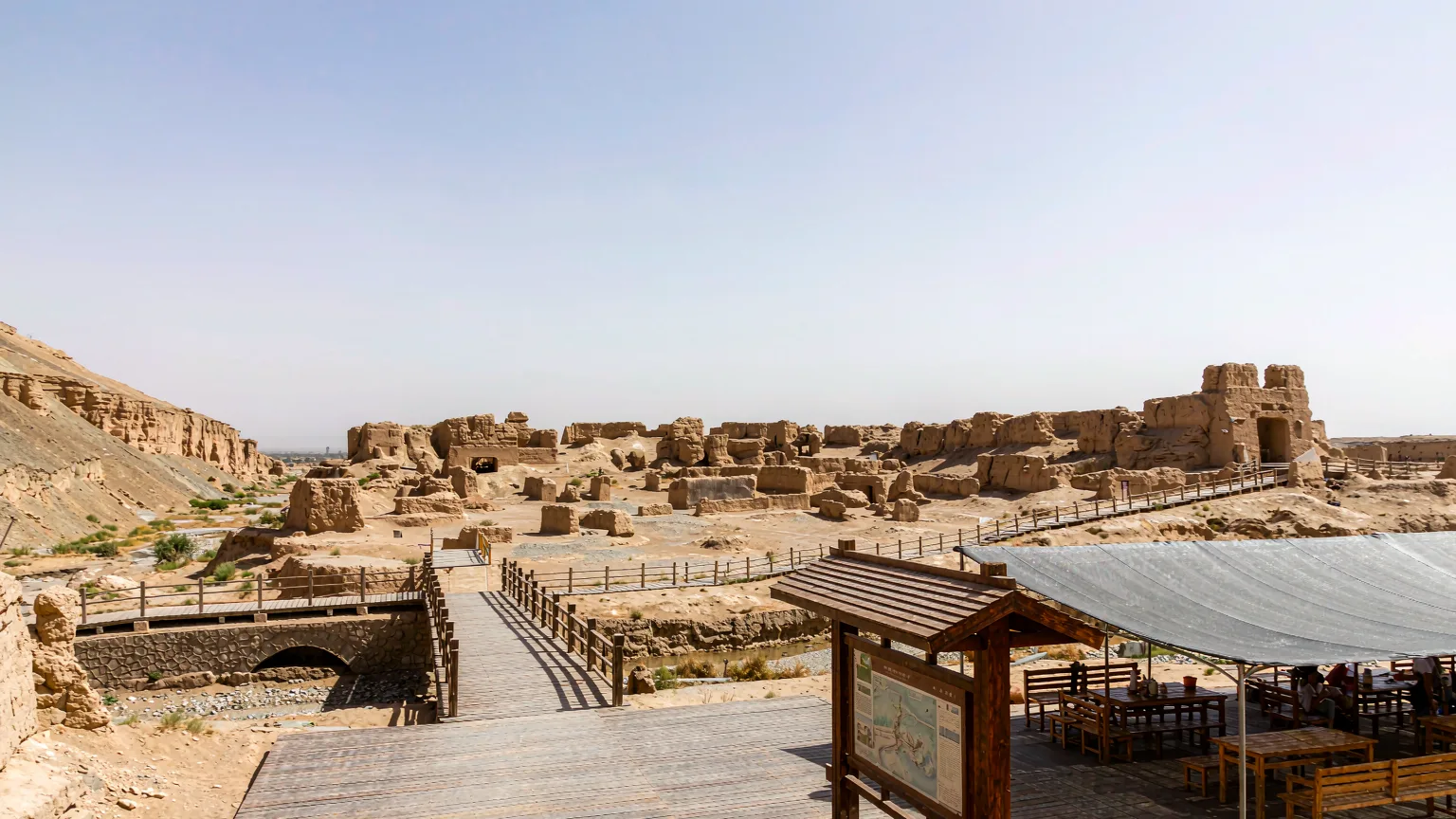 Visitor on boardwalk entering Jiaohe Ancient City with guide and ruins ahead