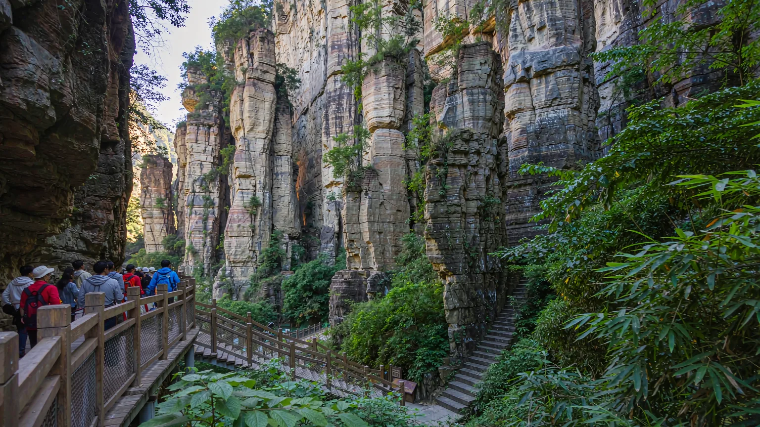 Wooden boardwalk trail with hikers overlooking Jinjiang Grand Canyon's rock pillars