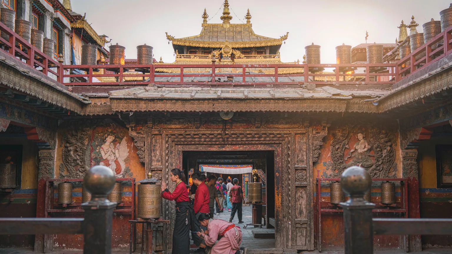 Tibetan pilgrims prostrating at Jokhang Temple entrance courtyard with prayer wheels