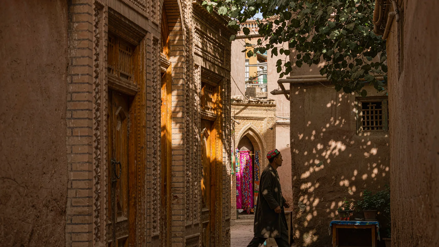 Narrow mud-brick alley in Kashgar Old Town with a Uyghur man walking