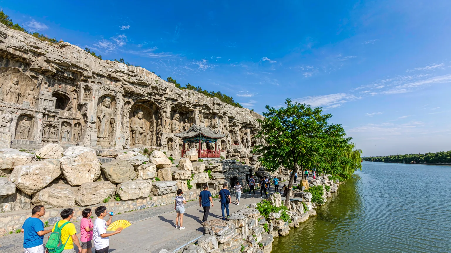 Visitors walking along pathway beside Yi River at Longmen Grottoes