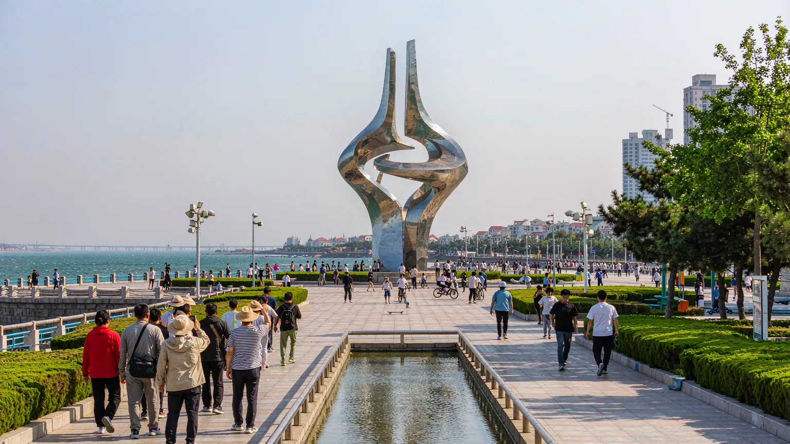Tourists walking along seaside promenade toward May Wind sculpture