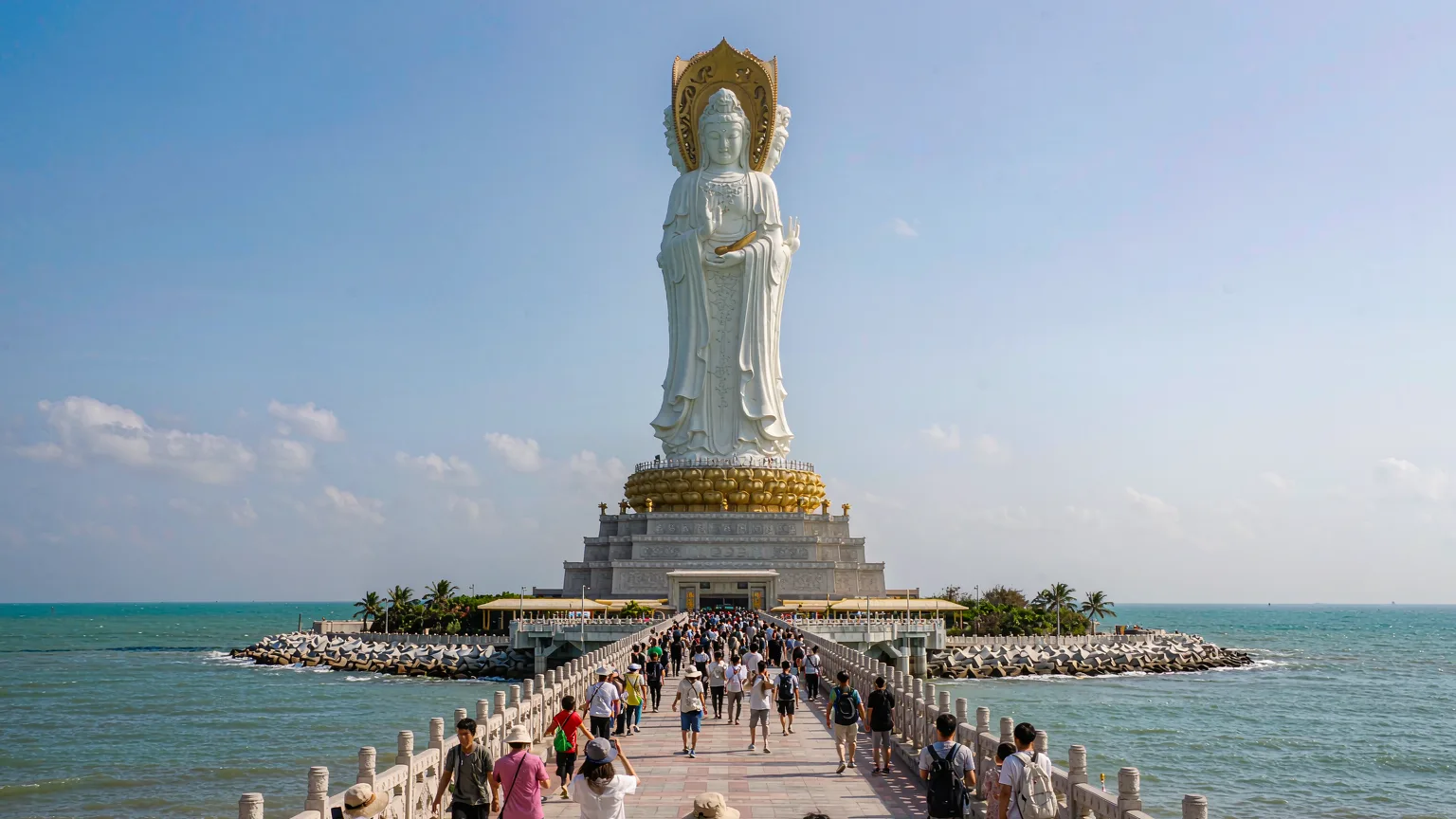 Tourists walking on bridge toward the giant Guanyin statue