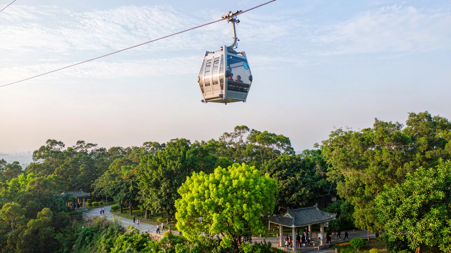 Cable car ascending over forested Qingxiu Mountain with visitors and entrance below