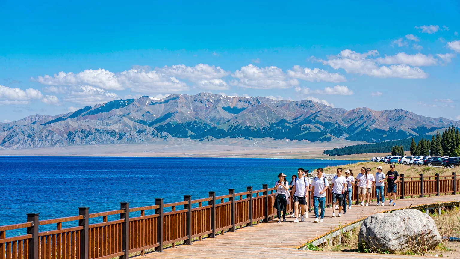Tourists on boardwalk by Sayram Lake with mountains in background