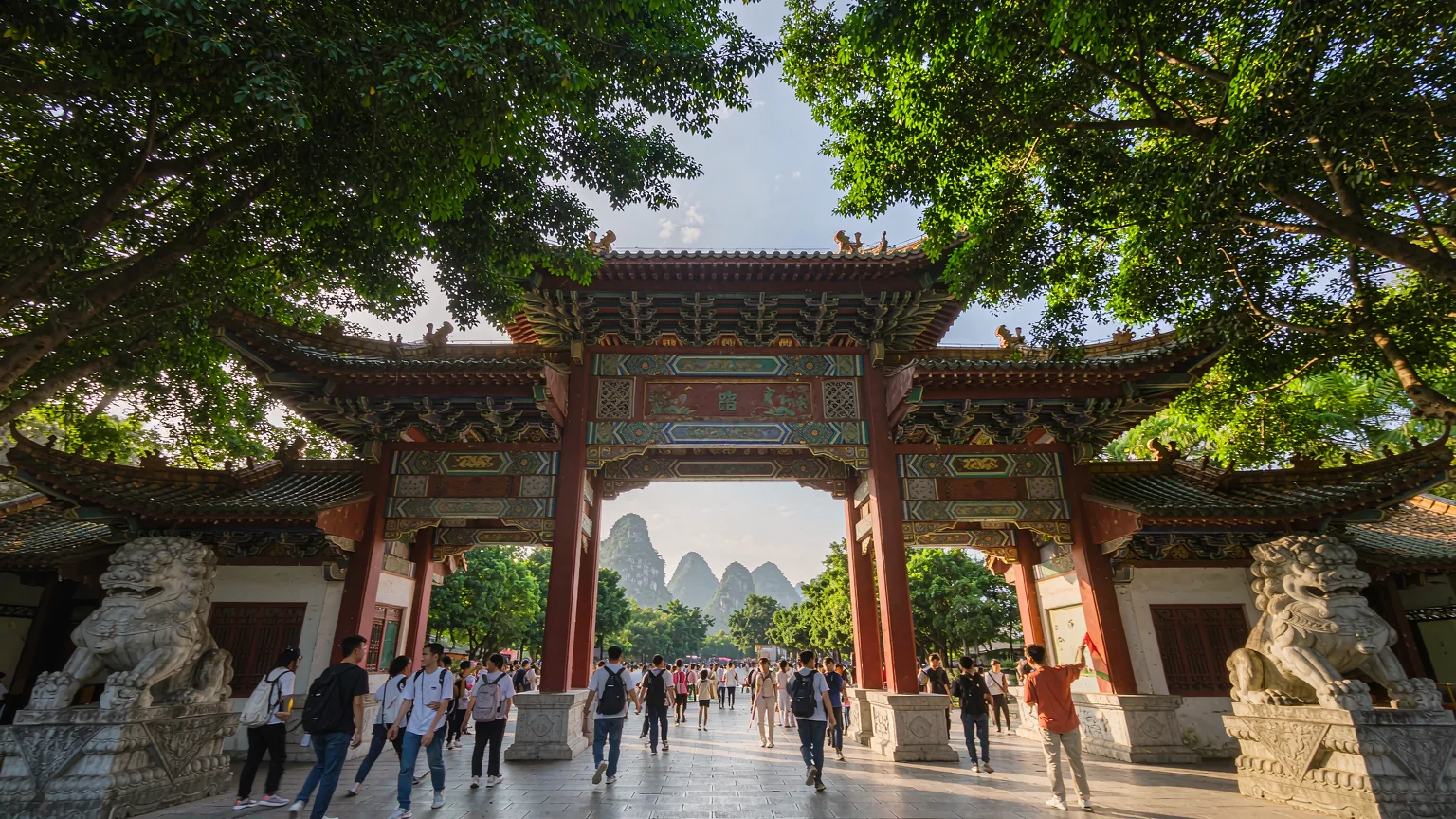 Tourists entering Seven Star Park through a traditional Chinese gate with stone lions
