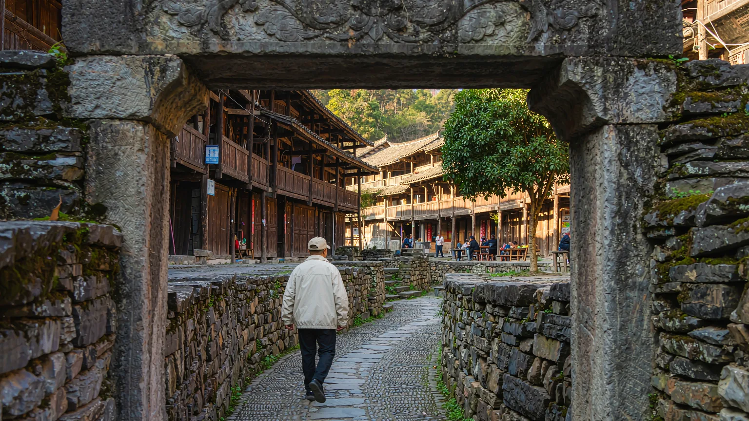 Traveler entering Shaxi Ancient Town through stone gate onto cobblestone path