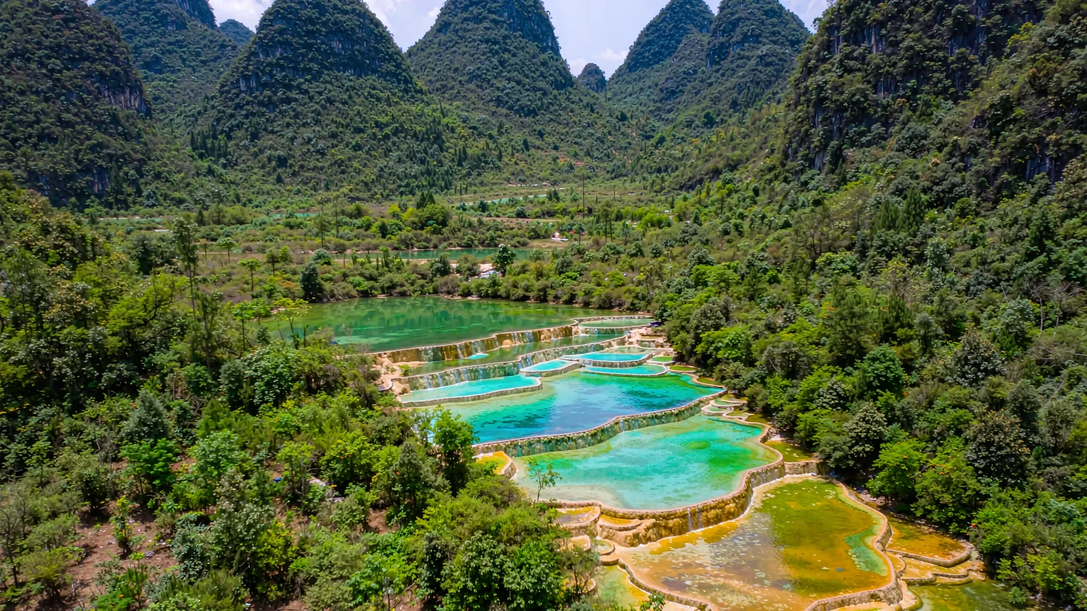 Colorful travertine terraces of Shenxianchi surrounded by dense forest and mountains