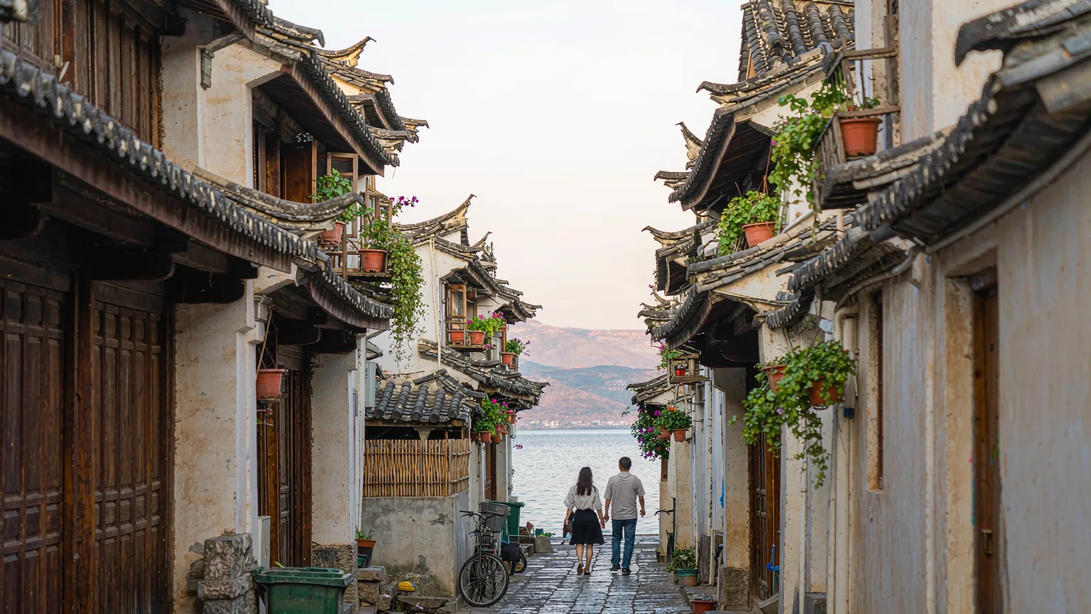 Visitors walking through a narrow stone alley in Shuanglang Ancient Town with Bai architecture