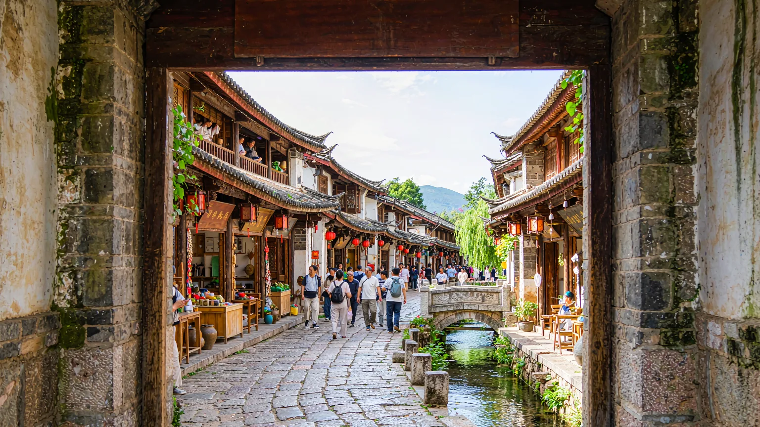 Tourists entering Shuhe Ancient Town via stone gate and bridge
