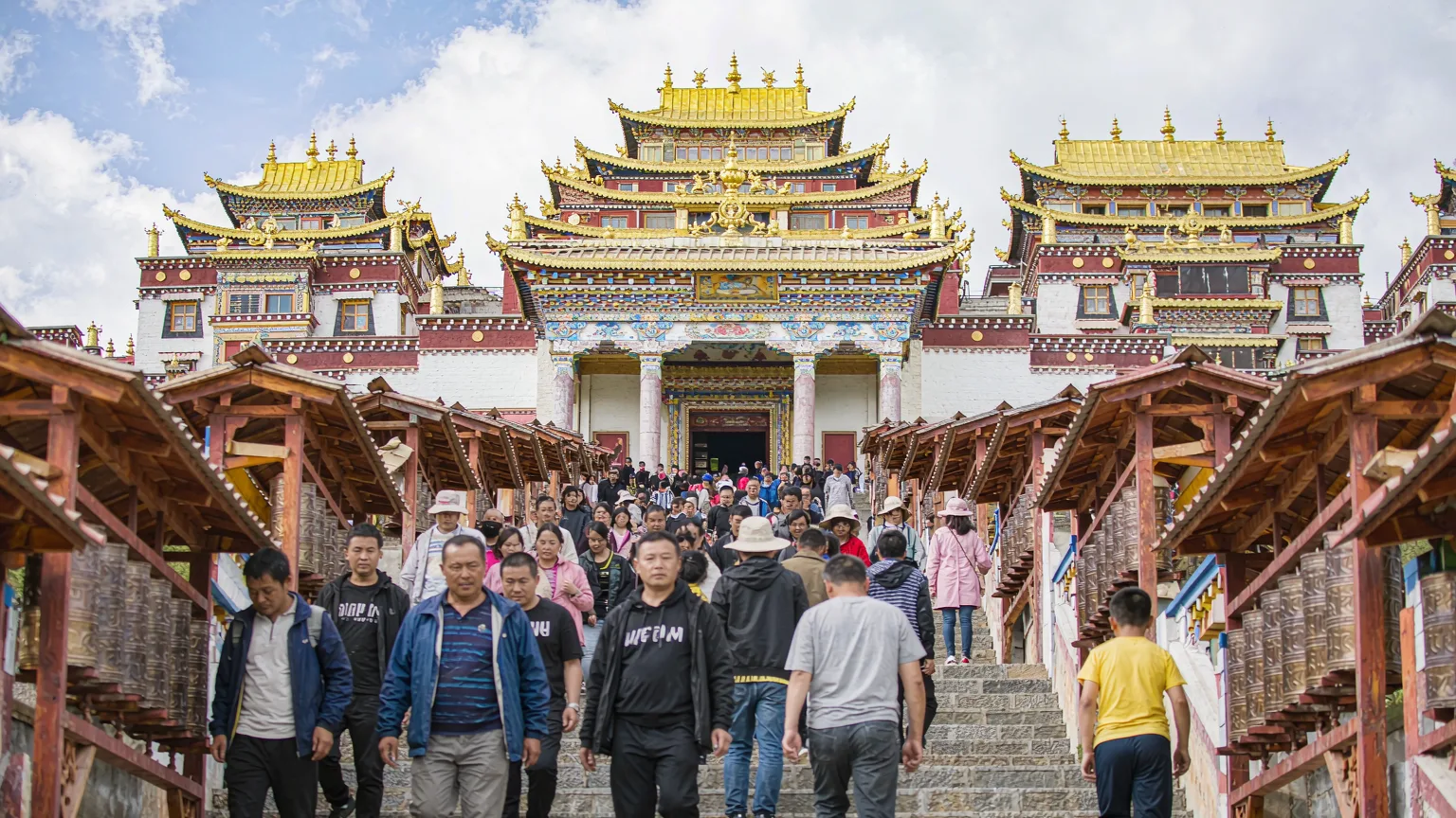 Pilgrims ascending stone stairs to Songzanlin Monastery's entrance with prayer wheels