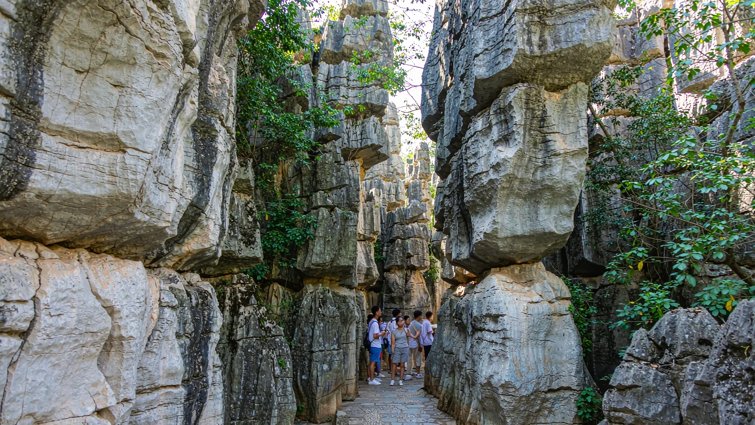 Visitors walking a stone path between towering limestone pillars in Shilin