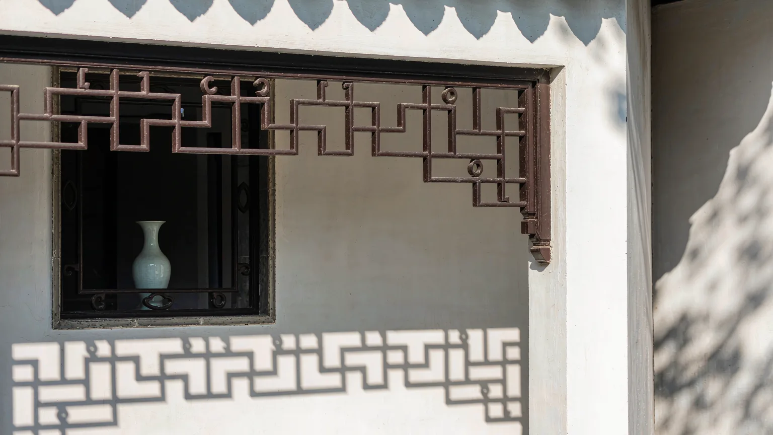 Intricate geometric window lattice in Suzhou Museum casting shadows on a white wall.