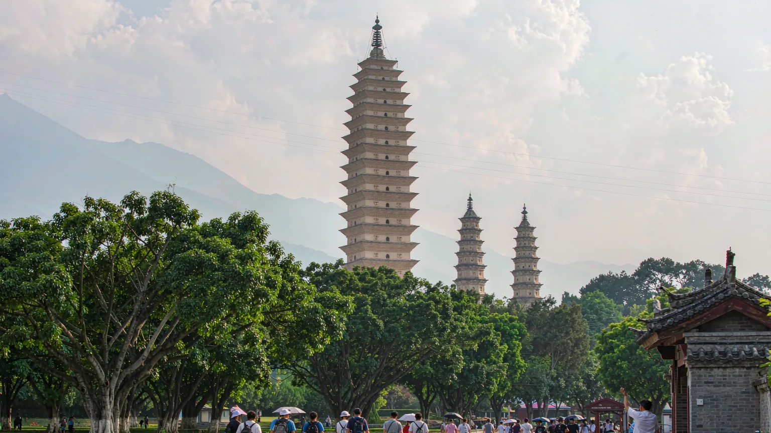 Tourists walking toward the Three Pagodas through a tree-lined entrance path