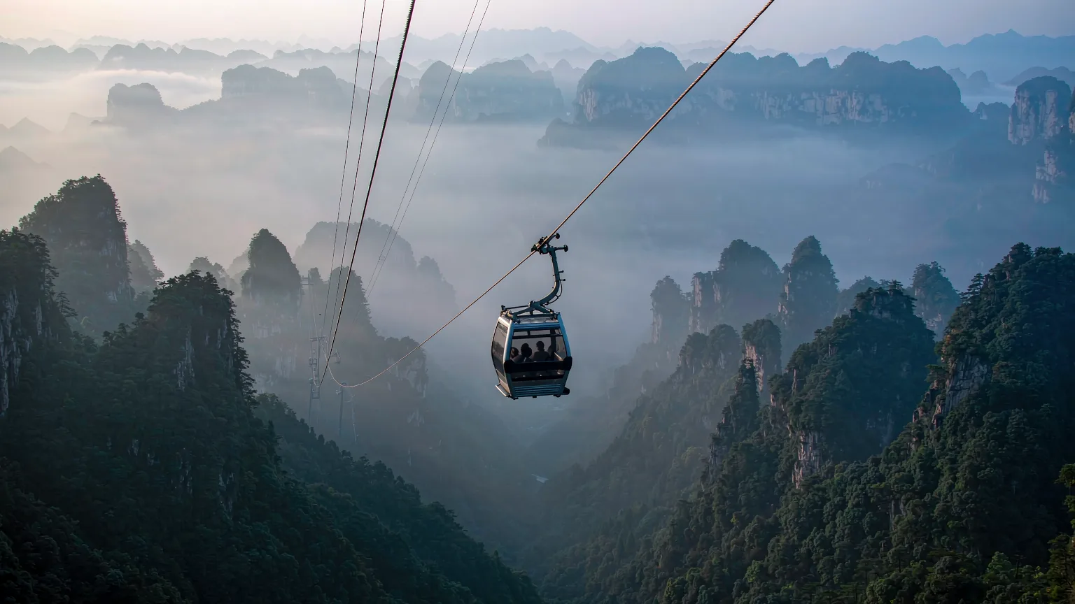 Cable car cabin soaring above forested ridges toward Tianmen Mountain summit