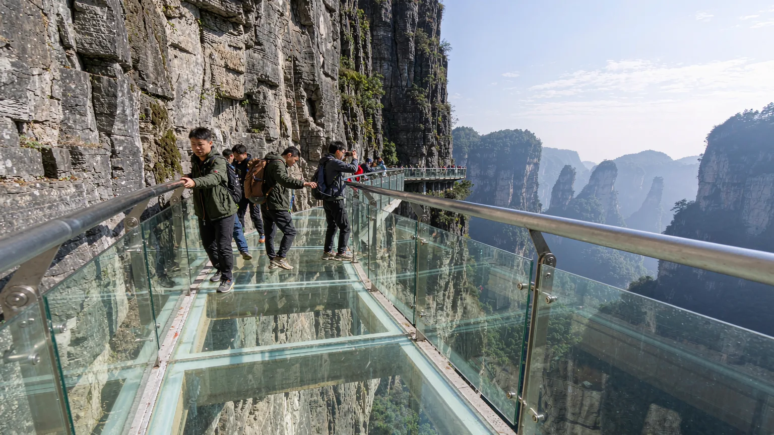 Tourists on glass skywalk clinging to Tianmen Mountain's vertical cliff face