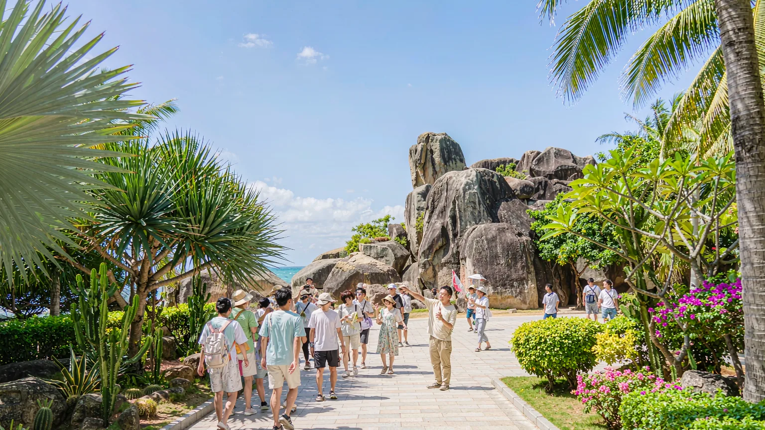 Tourists walking on pathway towards Tianya Haijiao boulders with guide
