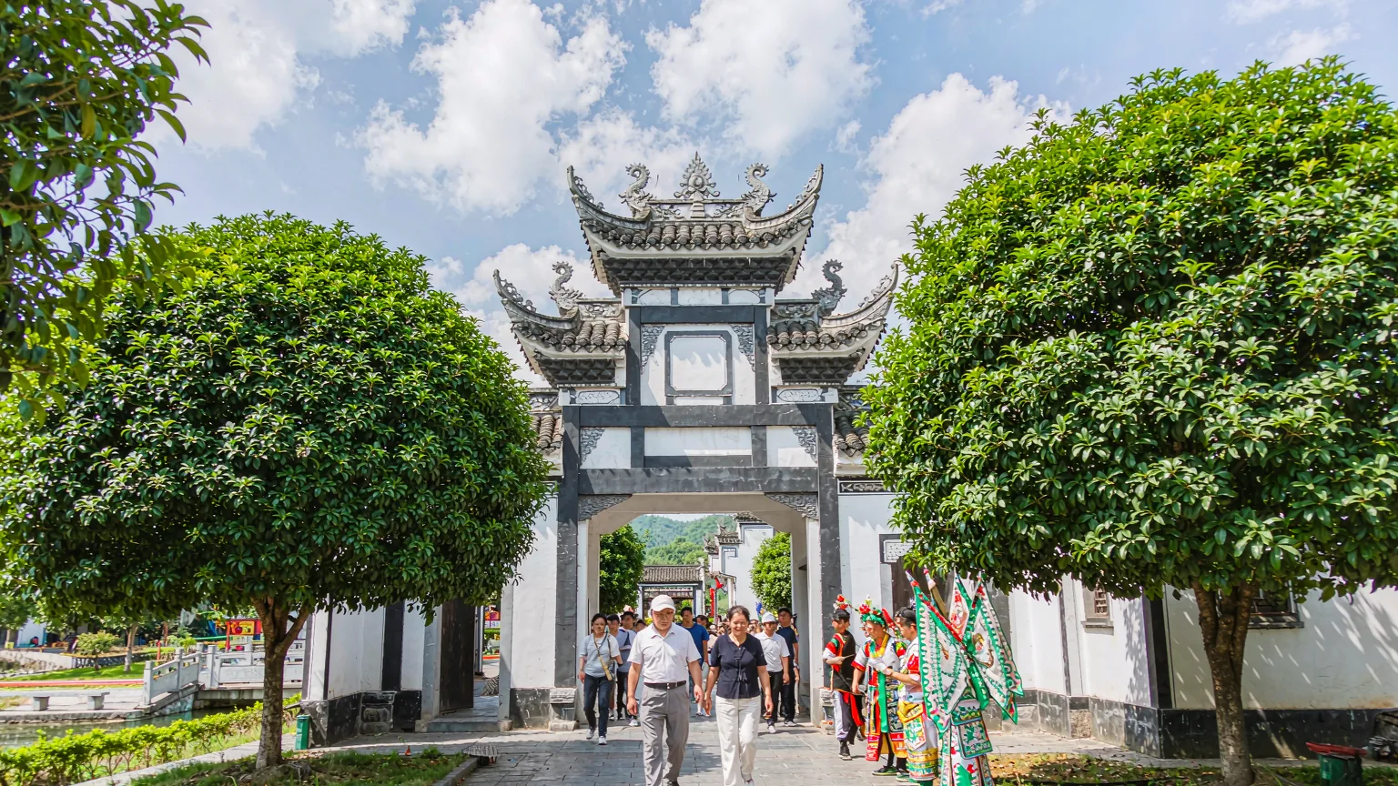 Visitors entering Tujia Folk Custom Park through ornate gate with performers
