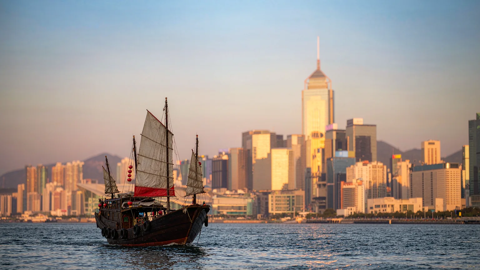 Traditional junk boat sailing past modern skyscrapers on Victoria Harbour
