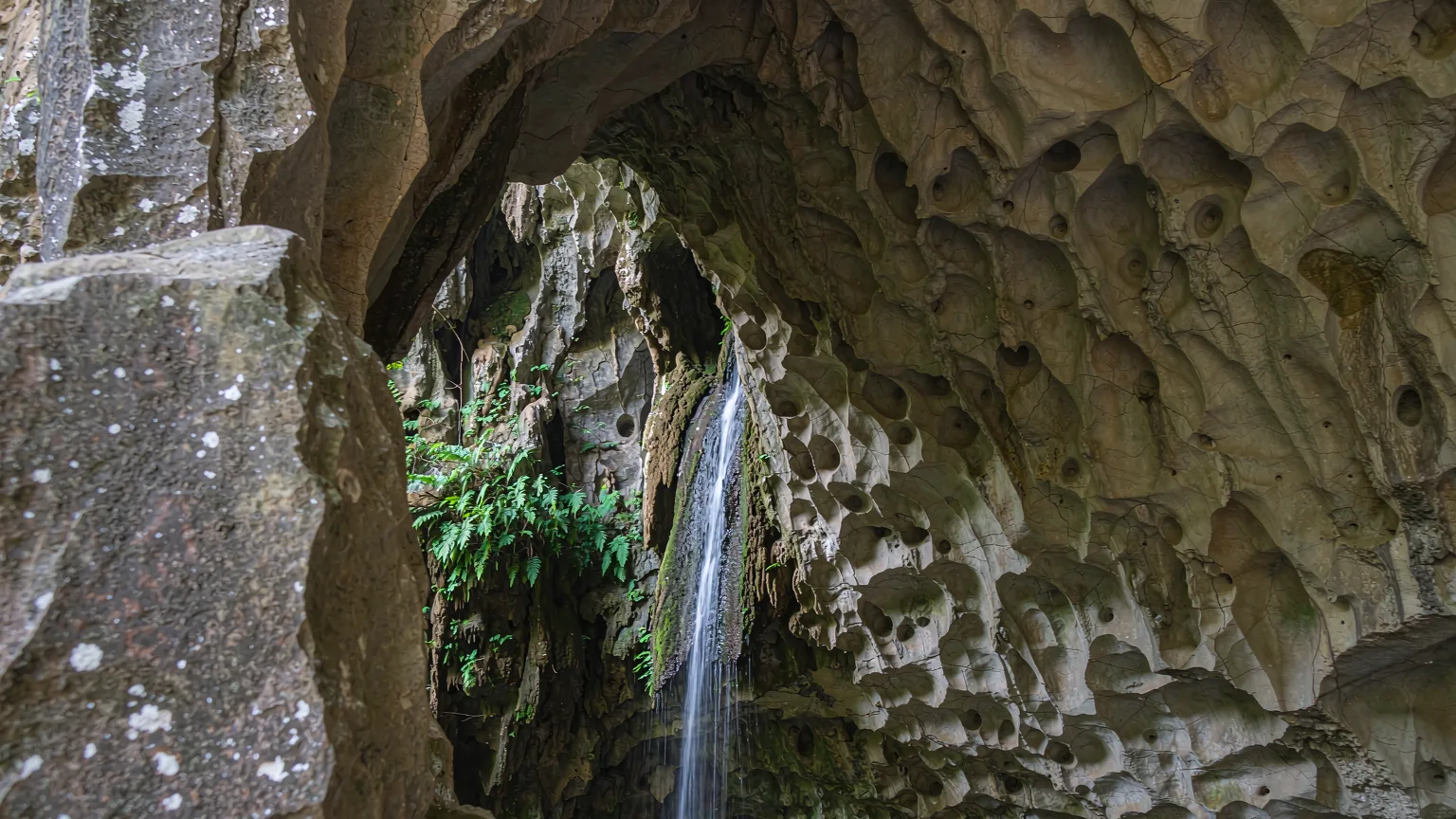 Close-up of ancient limestone arch with waterfall and moss at Wulong