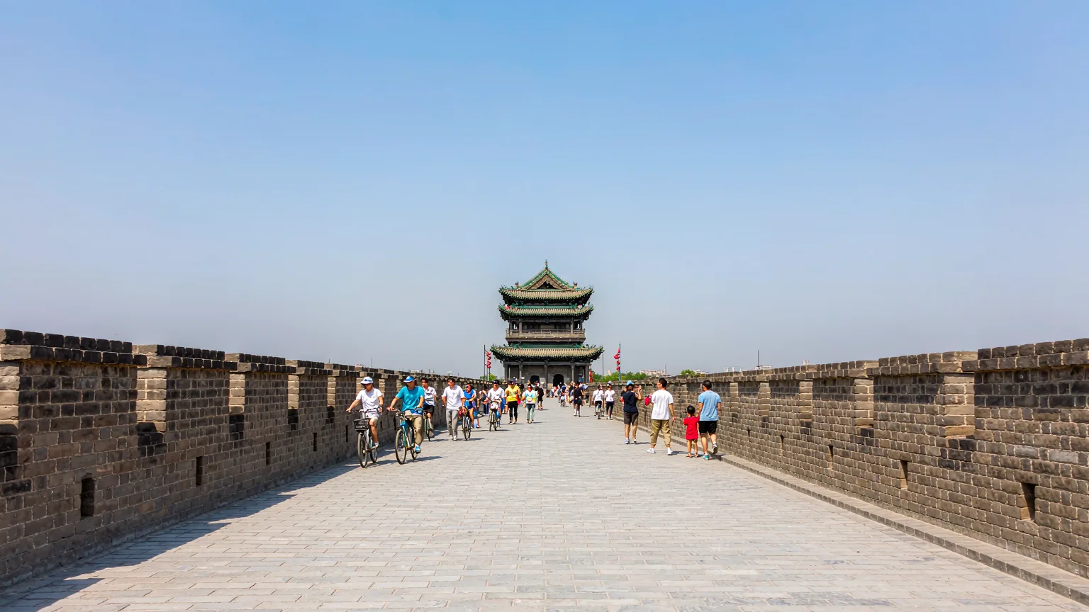 Walkway atop Xi'an City Wall with cyclists and crenellations under blue sky