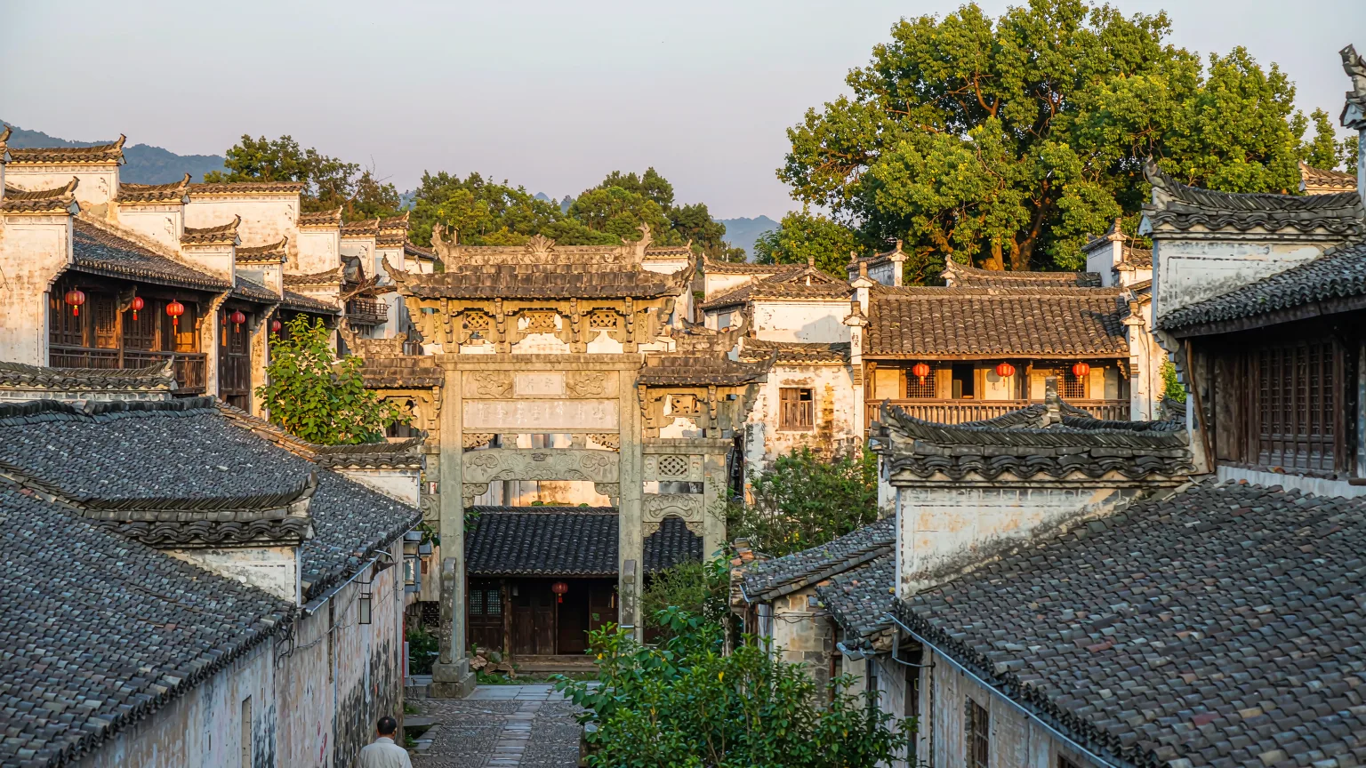 Visitor walking through Xidi's main street under a carved stone gate