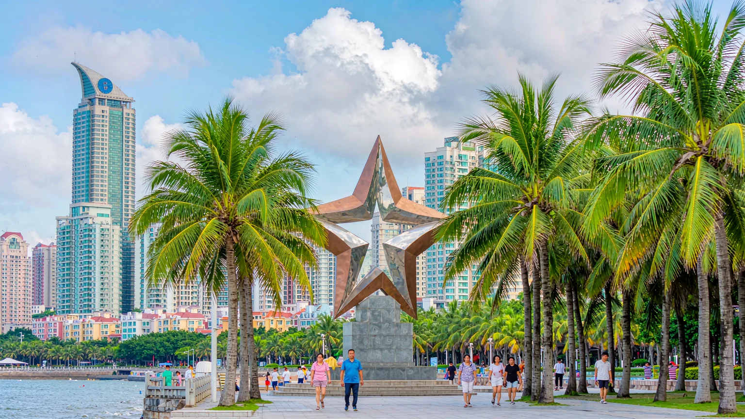 People strolling on Xinghai Square promenade with monument behind