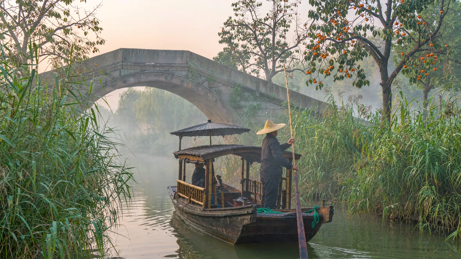 Wooden boat with fisherman on a narrow reed-lined canal in Xixi Wetland
