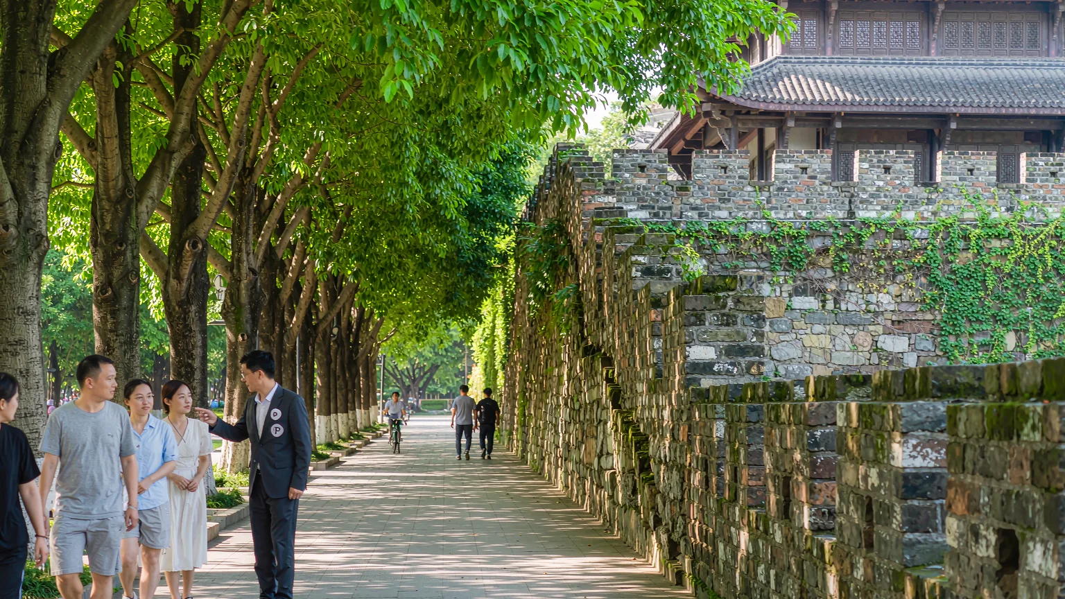 Tourists walking on a shaded path beside the Ming city wall in Yuexiu Park