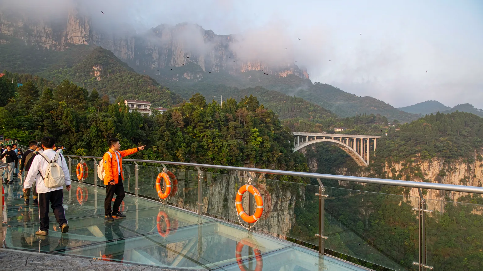 Tourists stepping onto the glass deck of Zhangjiajie Grand Canyon Bridge with a guide