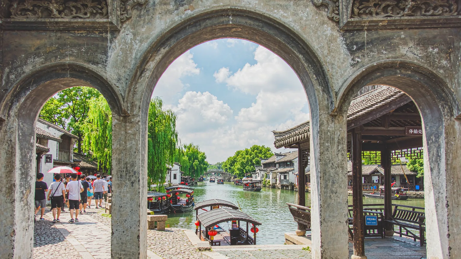 Tourists entering Zhouzhuang Ancient Town via stone archway and canal dock
